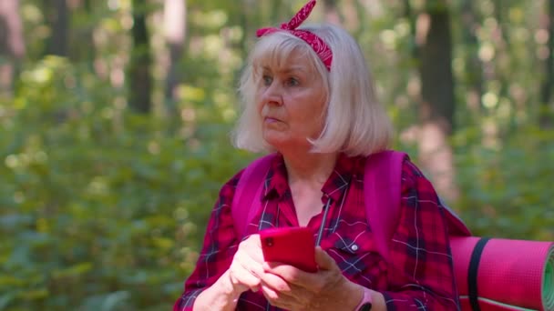 Attraktiv äldre gamla mormor kvinna backpacker planerar resa i skogen på mobiltelefon — Stockvideo