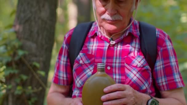Zmęczony spragniony starszy, stary kaukaski wędrowiec dziadek relaksujący się, pijący wodę w lesie po spacerze — Wideo stockowe