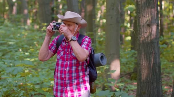 Senior man grootvader op wandeltocht het verkennen van wilde dieren nemen van foto 's in het bos met retro camera — Stockvideo