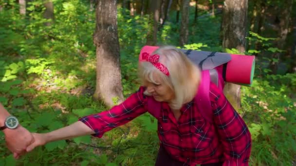 Starsza kobieta na hikinig przygoda podróż trzymając mans rękę pomaga jej wspiąć się na wzgórzu górskim w drewnie — Wideo stockowe