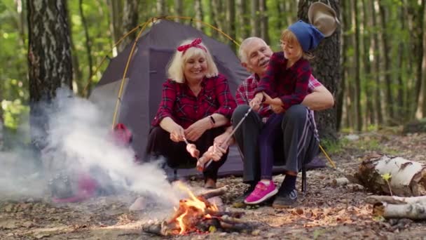 Senior babička dědeček s vnučkou vaření párky nad táborák ve dřevě — Stock video