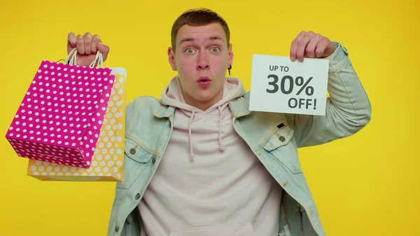 Fröhlicher Teenie-Mann zeigt Einkaufstüten und bis zu 30 Prozent Rabatt auf Aufschriften, Black Friday — Stockfoto
