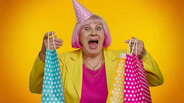 Anciana abuelita mostrando bolsas de compras, descuentos publicitarios, mirando sorprendido con precios bajos — Foto de Stock