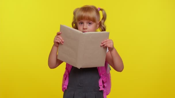 Lächelndes Schulmädchen, das sich hinter einem Buch versteckt, lacht herum und macht verspielte alberne Mimik — Stockvideo