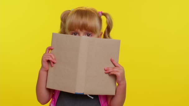 Lovely teenage girl kid in school uniform wears pink backpack peeping while hiding behind a book — Stock Video