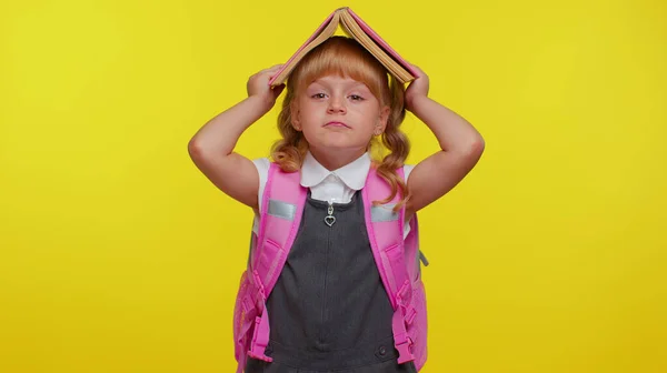 Vrolijk schattig leuk grappig schoolmeisje kind met boek op het hoofd, het maken van speelse domme gezichtsuitdrukkingen — Stockfoto