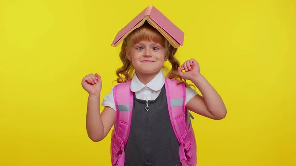 Fröhlich niedlich glücklich lustig Schulmädchen Kind mit Buch auf dem Kopf, macht spielerisch dumme Mimik — Stockfoto