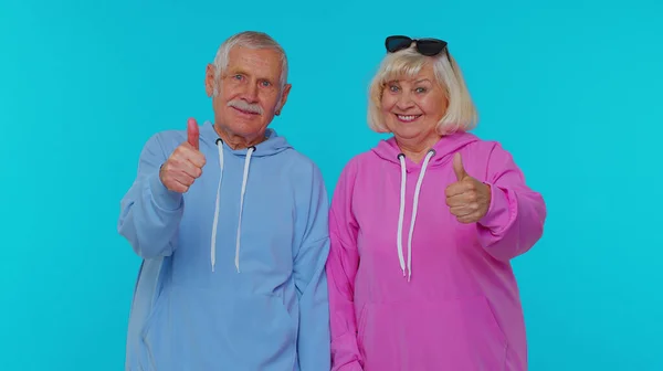 Senior stylish grandparents pensioners looking approvingly at camera showing thumbs up, like sign