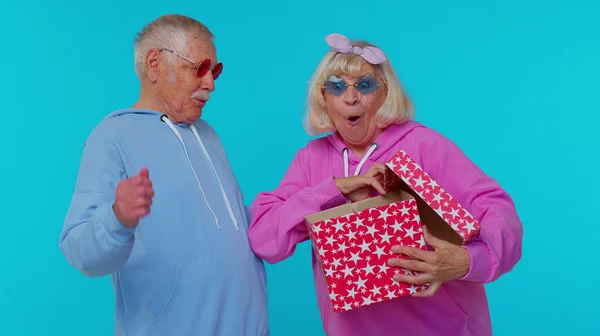 Веселая пожилая пара мужчина женщина бабушка с дедушкой открывая подарочную коробку, улыбаясь радостно день рождения сюрприз — стоковое фото
