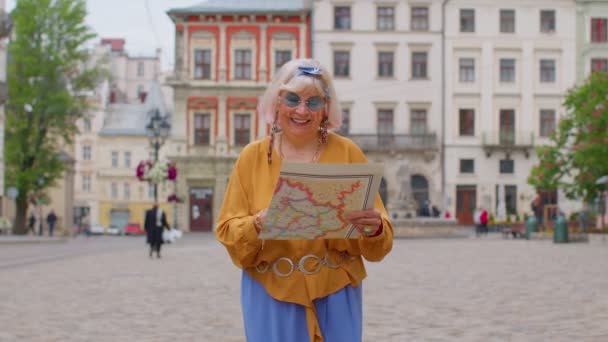 Äldre eleganta turist mormor kvinna promenader längs gatan, letar efter sätt att använda papperskarta i staden — Stockvideo