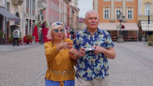 Yaşlı, şık turistler, kadın ve erkek eski film kameralarıyla fotoğraf çekiyorlar, şehir caddesinde yürüyorlar. — Stok video
