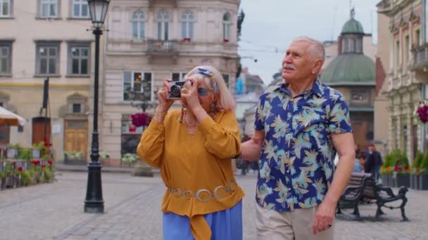 Старшие старые стильные туристы мужчина женщина ходьба, фотографируя на старую камеру в центре города летом — стоковое видео