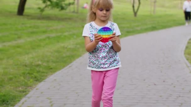 Дитяча дівчина стискає преси барвистий антистресовий сенсорний екран штовхає популярну іграшку в парку — стокове відео