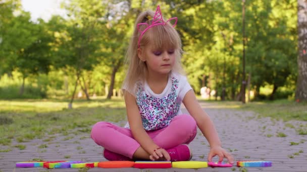 Gyermek lány gyerek játszik szorító anti-stressz pop it érintőképernyős játékok egyszerű gödröcske játék a parkban — Stock videók