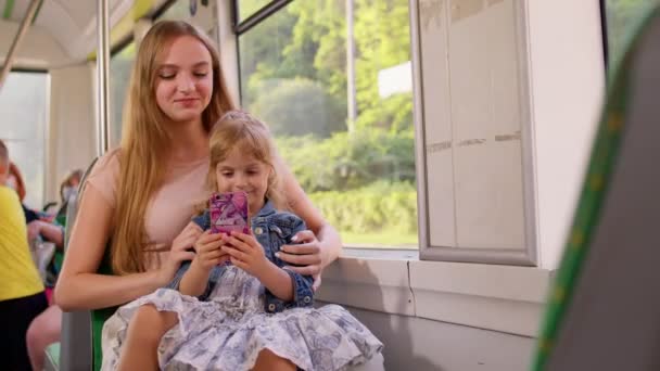 Menina criança com a mãe usando o aplicativo de rede social de internet do telefone móvel enquanto viaja de ônibus — Vídeo de Stock