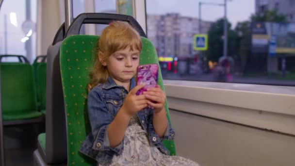 Şehre tramvayla seyahat ederken akıllı telefondan oynayan, mesajlaşan, sosyal medyada gezinen bir kız — Stok video