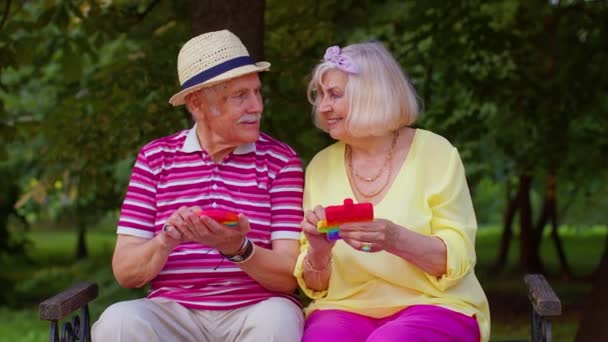 Улыбающийся дедушка старой бабушки, играющий анти-стрессовый сенсорный экран, толкает популярную игрушку — стоковое видео