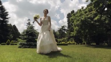 Beyaz gelinlik ve duvak içinde güzel bir gelin parktaki düğün buketini tutuyor.