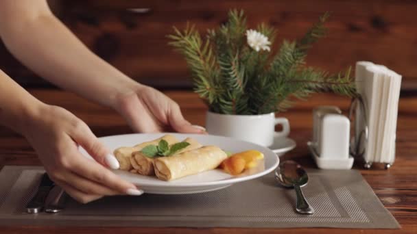 손으로 흰 접시에 맛있는 야채 바나나 복숭아 팬케이크를 얹고, 식당에서 아침 식사를 한다 — 비디오