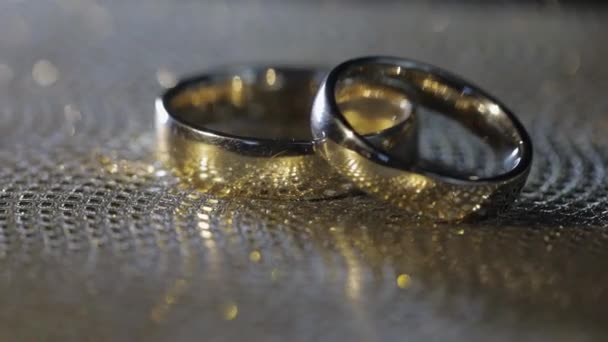 결혼식 반지가 놓여 있고, 돌고, 빛나는 황금빛 표면 위에서 빛을 반사하고, 확대 한 매크로 — 비디오
