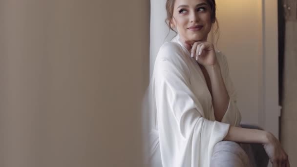 Novia en vestido de tocador cerca de la ventana, preparativos para la mañana de la boda, mujer en vestido de noche y velo — Vídeo de stock