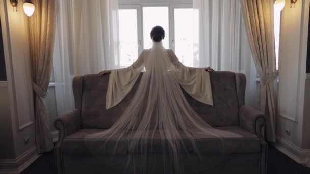 Novia en vestido de tocador cerca de la ventana, preparativos para la mañana de la boda, mujer en vestido de noche y velo — Vídeo de stock