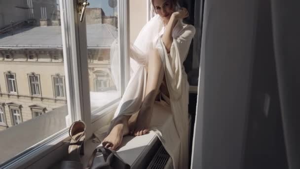 Pengantin dalam gaun kamar kerja duduk di jendela sill pernikahan pagi persiapan wanita dalam gaun malam, kerudung — Stok Video