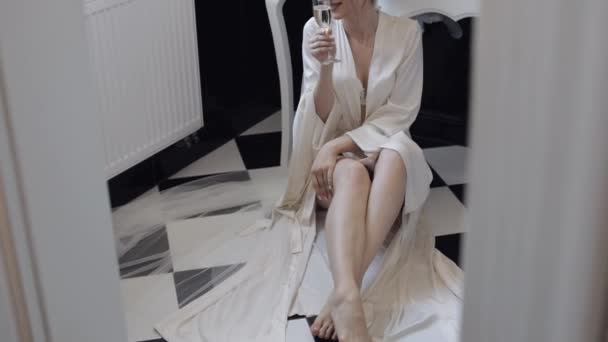 Braut im weißen Boudoir-Kleid sitzt auf dem Boden im Badezimmer zu Hause Wohnung mit einem Glas Champagner — Stockvideo