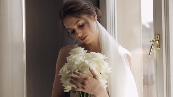 Noiva em vestido branco ficar perto da janela com buquê de flores, preparações da manhã do casamento em casa — Vídeo de Stock