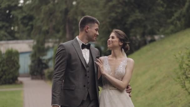 Gyönyörű friss házasok kaukázusi menyasszony vőlegény séta a parkban, kéz a kézben, esküvő pár család — Stock videók