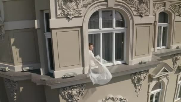 Νύφη σε μπουντουάρ φόρεμα κάθεται στο περβάζι παράθυρο γάμο πρωινές προετοιμασίες γυναίκα σε νυχτικό, πέπλο — Αρχείο Βίντεο