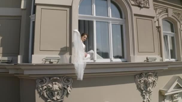 Sposa in abito boudoir seduto sul davanzale della finestra preparativi del mattino di nozze donna in abito da notte, velo — Video Stock