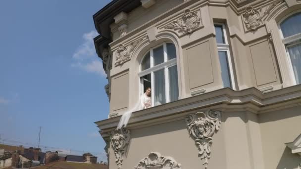 Novia en vestido de tocador sentado en el alféizar de la ventana preparativos de la boda mujer en vestido de noche, velo — Vídeo de stock