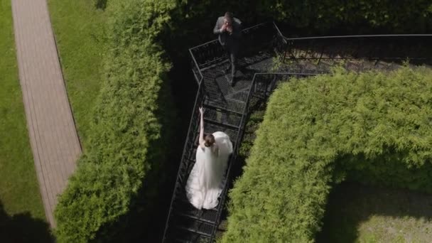 Молодожены, кавказский жених с невестой остаются на лестнице в парке, супружеская пара, мужчина и женщина влюблены — стоковое видео