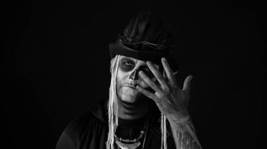 Korkunç cadılar bayramı makyajlı ürkütücü adam yüzünü asıyor, elinin arkasına saklanıyor.