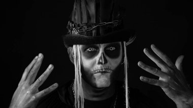 Korkunç cadılar bayramı makyajlı ürkütücü adam yüzünü asıyor, elinin arkasına saklanıyor.