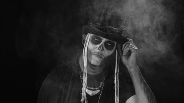 Şapkalı, iskelet makyajlı ürkütücü bir adam. Adam surat yapıyor, dişlek gülüyor. Cadılar Bayramı tematik partisi