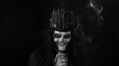 Şapkalı, iskelet makyajlı ürkütücü bir adam. Adam surat yapıyor, dişlek gülüyor. Cadılar Bayramı tematik partisi