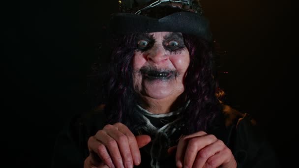 Страшная пожилая женщина с хэллоуинским макияжем, смотрящая в камеру, пытаясь напугать, улыбаясь — стоковое видео