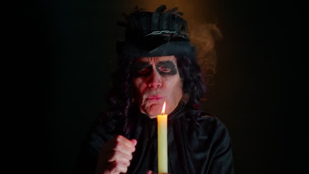 Hombre mayor siniestro en traje de carnaval de bruja de Halloween sopla humo de la boca, tratando de asustar — Vídeo de stock