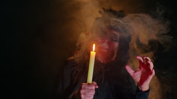 Hombre siniestro con maquillaje de bruja de Halloween aterrador en traje haciendo rituales mágicos de vudú con vela — Vídeos de Stock