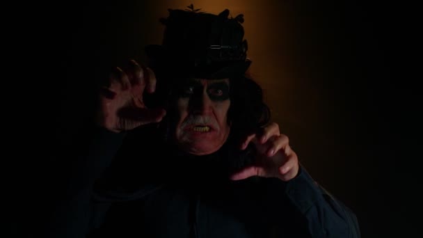 Hombre mayor aterrador con maquillaje de bruja de Halloween mirando a la cámara, tratando de asustar, mostrar la lengua — Vídeos de Stock