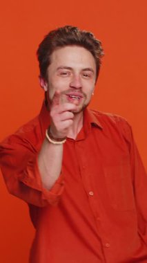 Komik beyaz adam kameraya dil gösteriyor, dalga geçiyor, şakalaşıyor, alay ediyor, alay ediyor, alay ediyor, kabadayılık ediyor, saygısızlık ediyor. Turuncu arka planda izole edilmiş yakışıklı genç adam.