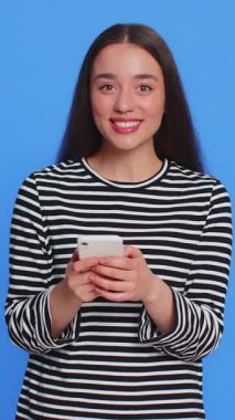 Beyaz bir kadının mesajlaşması akıllı telefon sosyal medya uygulamalarında içerik paylaşımı, rahatlama filmi izlemesi. Genç kız mavi arka planda izole edilmiş cep telefonu gülümsemesi kullanıyor.