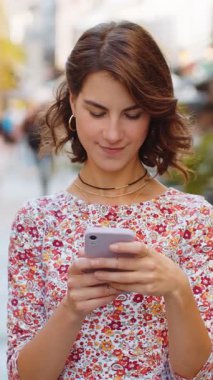 Akıllı telefon kullanarak gülümseyen genç bir kadın. Kısa mesajlar yazarak interneti tarıyor, işi bitiriyor, dışarıdaki kameralara bakıyor. Şehir caddesinde yürüyen bir kız turist. Kasaba yaşam tarzları