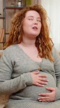 Hamile genç bir kadın kanepesinde oturup karnına hafifçe dokunuyor ve sevgi dolu bir ifadeyle yumuşakça konuşarak gelecekteki bebekle erken bir bağ kuruyor. Kız duygusal anları kucaklıyor, sıcak bakımı hissediyor.