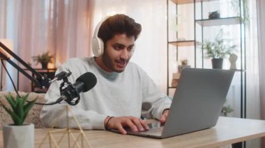 Bilgisayarda oynayan genç Hintli adam canlı yayın sırasında aktif olarak oyun etkinliklerine tepki veriyor, kulaklık, stüdyo mikrofonu kullanarak evdeki oturma odasındaki masada otururken vlog kaydediyor..