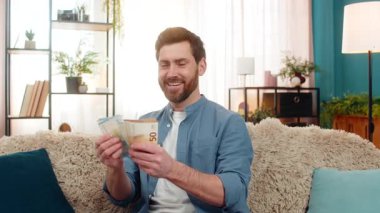 Evde elinde bir tomar nakit para tutan genç bir adam, heyecanla parayı sayıyor. Kanepede gülümseyen beyaz bir adam, büyük bir piyango kazanmasından ya da beklenmedik bir finansal başarıdan dolayı mutlu.