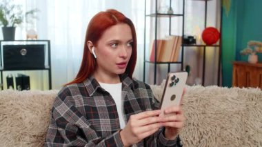 Evdeki genç kadın mobil uygulama kullanarak yeni bir dil öğreniyor ve kelimeleri odaklanma ve neşeyle yüksek sesle tekrarlıyor. Kanepedeki beyaz saçlı kız eğitim sürecinin tadını çıkarıyor. Telaffuz ve konuşma pratiği yapıyor.