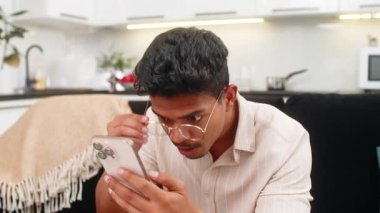 Evdeki Hintli adam akıllı telefondan gelen beklenmedik mesaja bakıyor gözlükleri çıkarıyor ve gözlerini kırpıyor. Kanepedeki Arap adam şaşkın hissediyor sonra rahatlamış bir gülümsemeyle gülüyor ve kısa bir sohbet ile cevap gönderiyor..